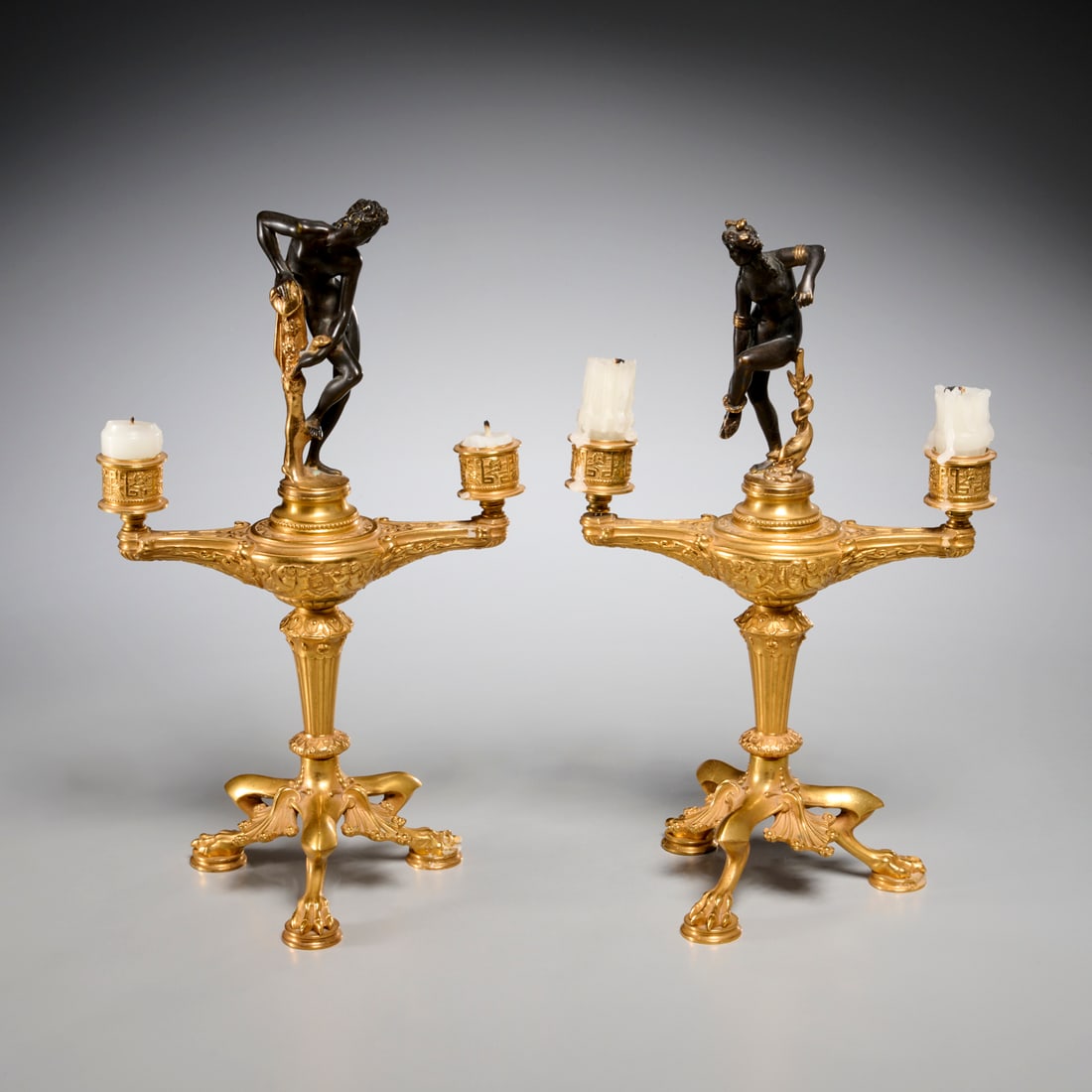 Pair Empire gilt and patinated bronze candelabra: Pair Empire gilt and patinated bronze candelabra, 19th c., France, the fluted tapering torch-form standard topped with two candle cups flanking a Neo-classical nude, raised on three animal legs ending