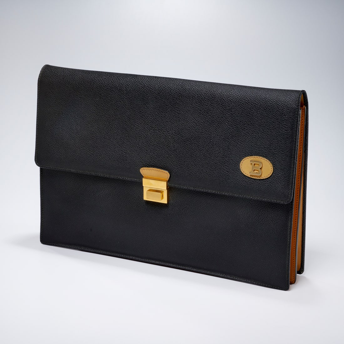 Bally bi-tonal portfolio attache: Bally bi-tonal portfolio attache, 20th c., Made in Italy, black pebbled leather with smooth camel calfskin, fold over flap style with gold hardware closure, logo B applied to flap, divided interior, a