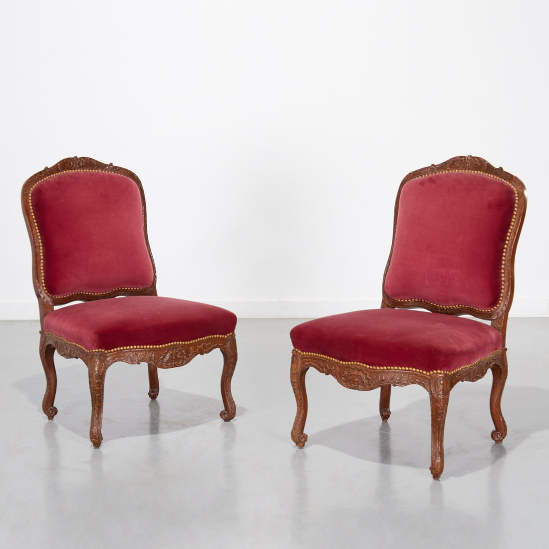 Pair Louis XV style beechwood chaises: Pair Louis XV style beechwood chaises, 19th c., France, the dark stained oak framed carved with floral scrolls, the padded back and seat upholstered in a red velvet, over serpentine skirt and cabriole