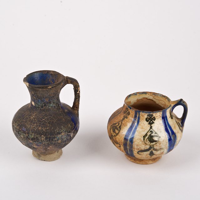 (2) Islamic glazed pottery juglets: (2) Islamic glazed pottery juglets: Poss. 13th c., incl. Rhages ware, 4.25"h x 3.25" (larger), 3"h x 3.75" (smaller) - Condition Report: overall fair/poor, crazing, mineral/lime deposits, glaze scratc