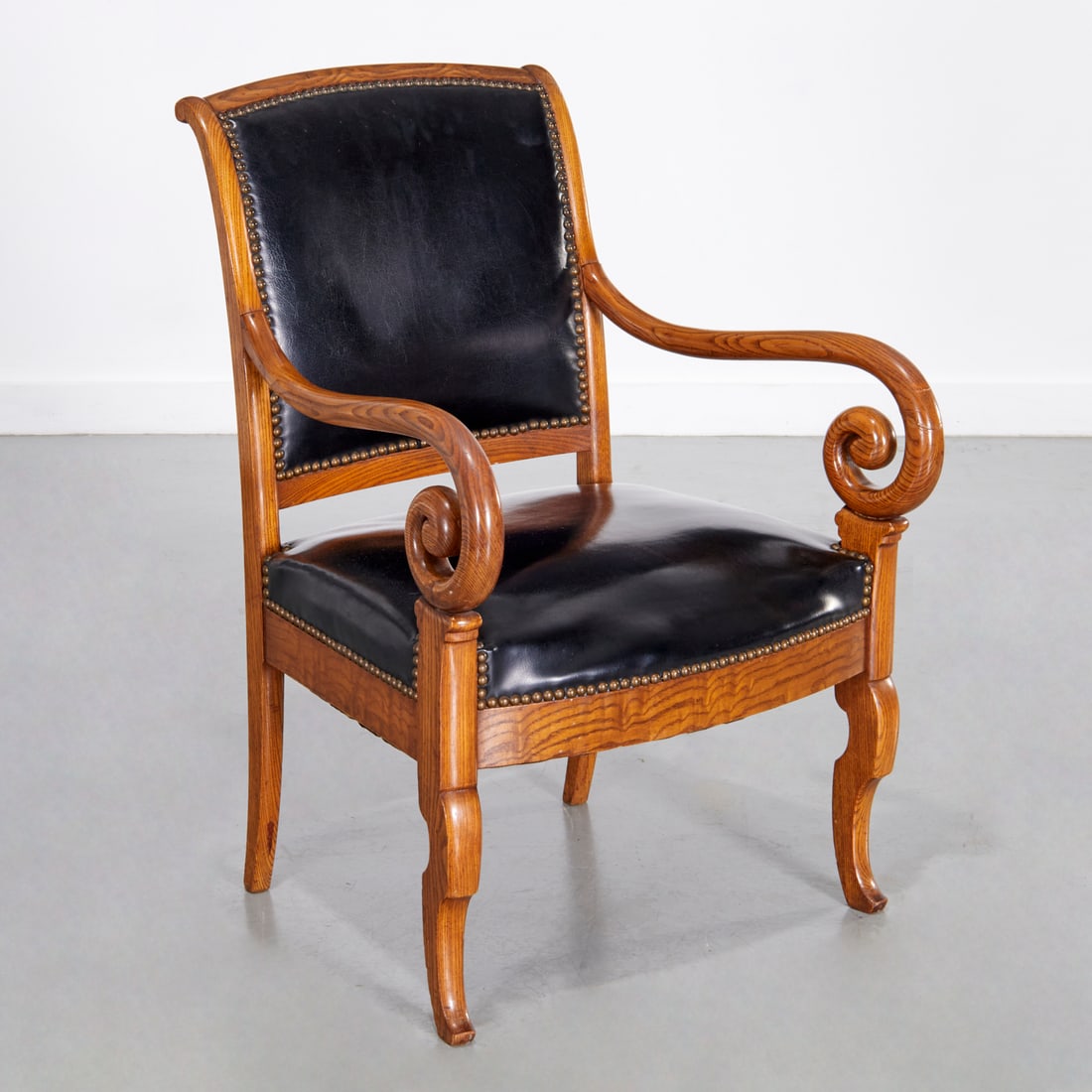 Empire style oak and leather fauteuil: Empire style oak and leather fauteuil, 19th/20th c., with scrolled arms and slight cabriole front legs, black leather upholstered seat and back, with nail head trim, 34.25"h x 23.5"w x 22"d