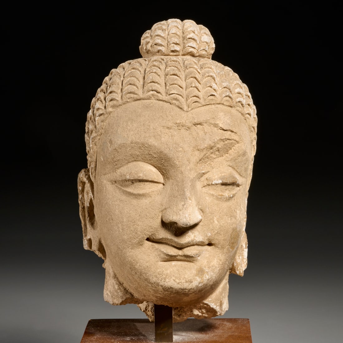 Gandaharan stucco head of Buddha: Gandaharan stucco head of Buddha, Possibly 4th/5th c. CE, depicted with serene expression, elongated earlobes, cranial protuberance "topknot", wavy locks of hair, drilled for mounting on slim post on 