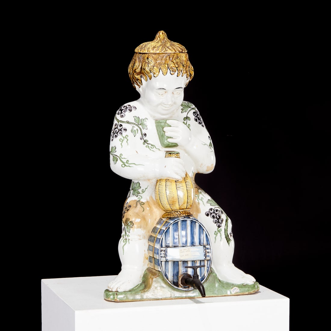 French faience figural wine cistern, ex Christie's: French faience figural wine cistern, ex Christie's, 18th c., modeled as Bacchus holding flask and cup, seated on barrel with brass spigot, decorated with fruiting vine along the body, Christie's lot s