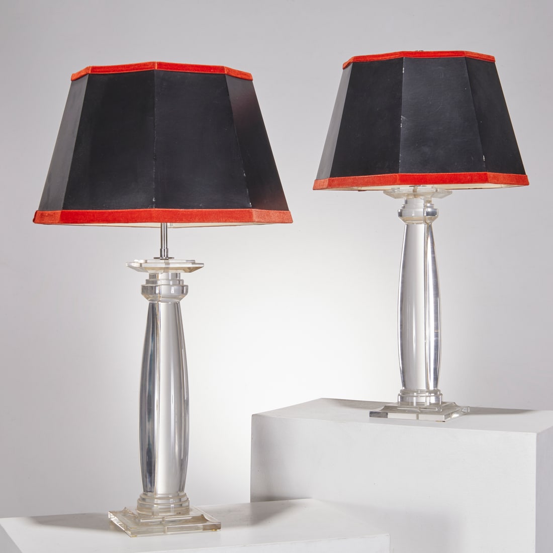 Pair Karl Springer (attrib) lucite table lamps: Pair Karl Springer (attrib) lucite table lamps, 20th c., column form, on beveled square base, black octagonal shades with red velvet trim, no signature observed, 30"h x 16"dia (total) Provenance: A Pr