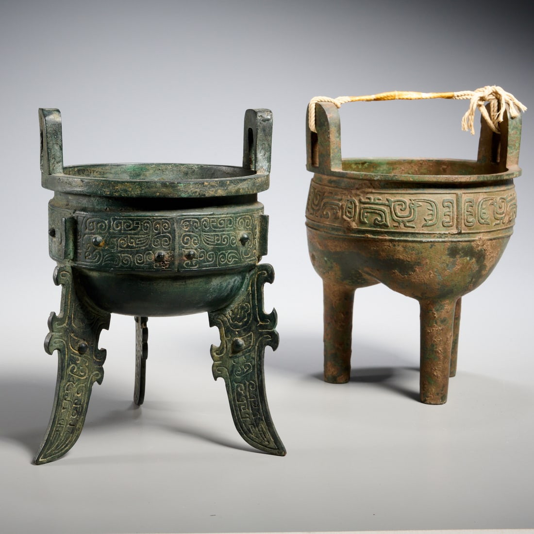(2) Chinese archaic style bronze tripod dings: (2) Chinese archaic style bronze tripod dings, Shang and Zhou Dynasty styles, China, each with twin upright handles, incised rim with archaic motifs, 9"h x 6.25"dia (larger), 8.75"h x 7"dia (smaller)