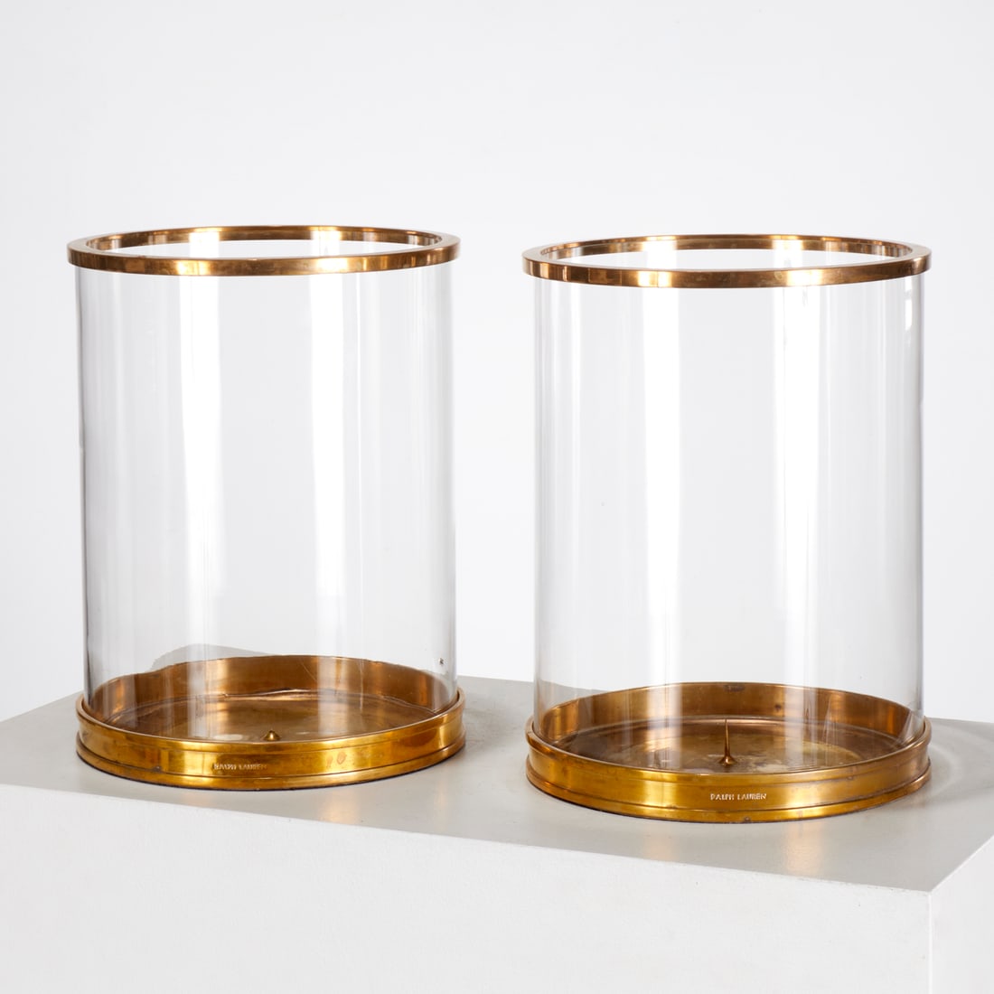 Pair Ralph Lauren brass mounted glass photophores: Pair Ralph Lauren brass mounted glass photophores, 20th/21st c., USA, cylindrical glass with brass rims and base, candle pricket interior, mark to side of base, each 11.75"h x 9"dia Provenance: A