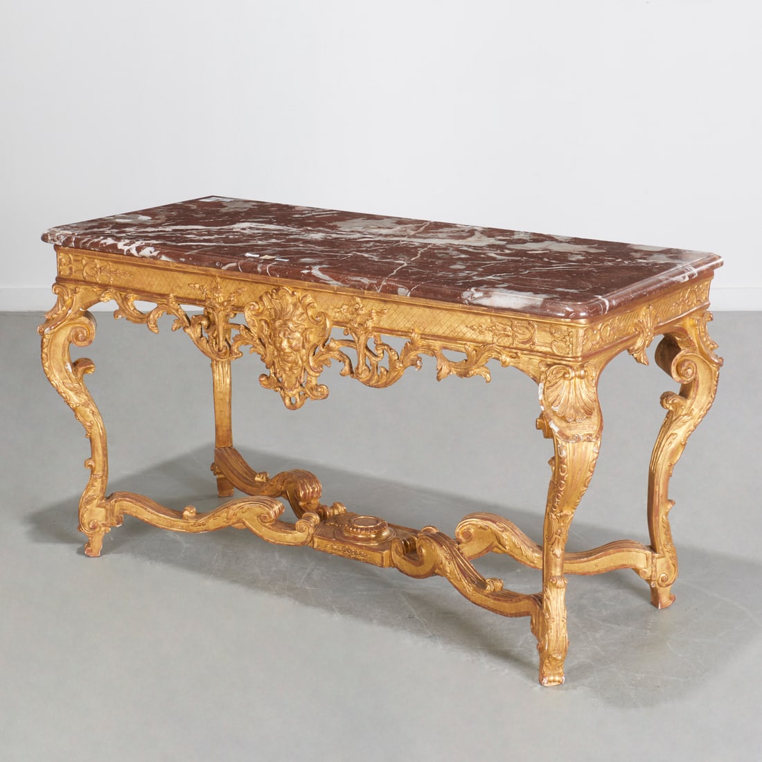 Regence giltwood marble top console: Regence giltwood marble top console, c. 1720, France, rouge Languedoc marble top on pierced apron centered with grotesque mask, the knees carved with shells, raised on cabriole legs joined by X-form s