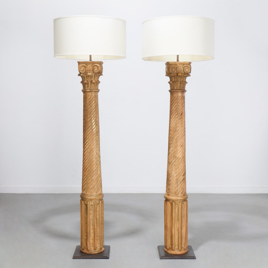 Pair Corinthian column carved wood floor lamps: Pair Corinthian column carved wood floor lamps, 20th c., Corinthian capital over spiral fluted shaft on square patinated steel base, unmarked, each 78"h x 12"squ Provenance: A Private Collection: