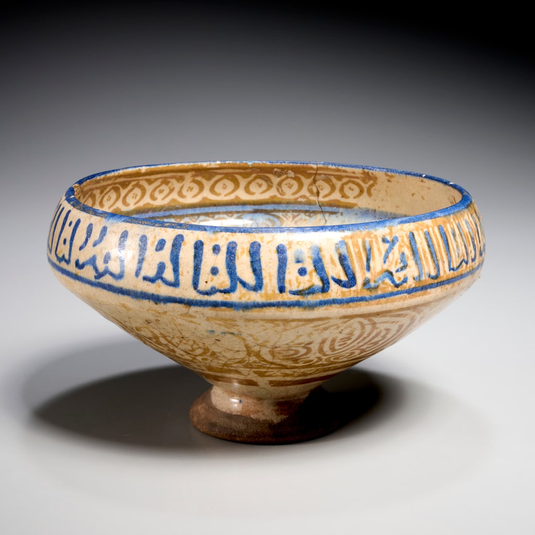 Antique Kashan pottery bowl, ex museum: Antique Kashan pottery bowl, ex museum, 13th c., Central Iran, blue and ochre decoration, the rim with Kufic script band, accession number inscribed and labeled verso, 4.75"h x 8.25"dia Provenance: Wo