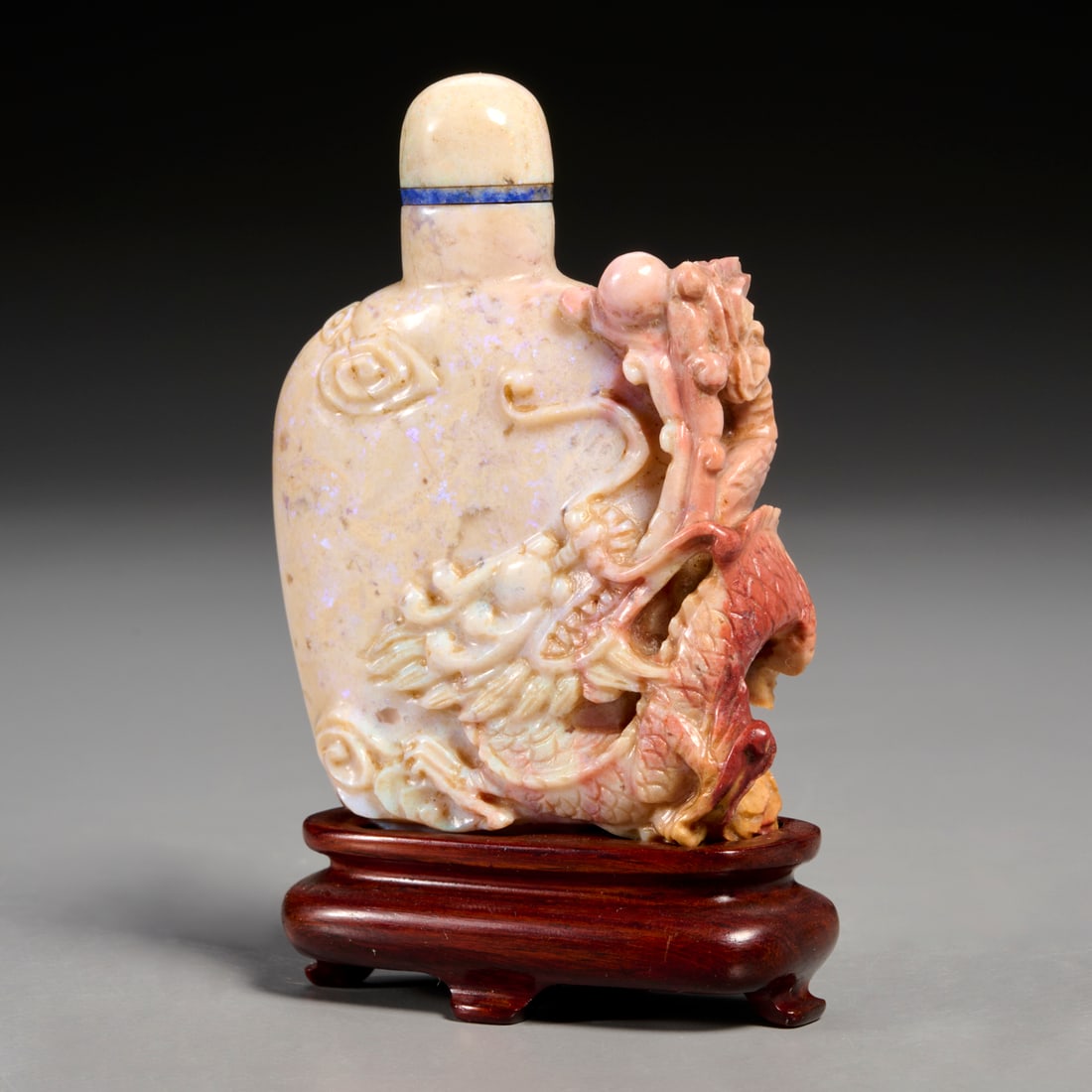 Chinese carved opal snuff bottle: Chinese carved opal snuff bottle, 20th c., fiery opal with specks fluorescing in purple and a few green, carved with dragon, lid with lapis ring, in custom form-fitting stand, 3"h x 2.25"w x .75"d (bo