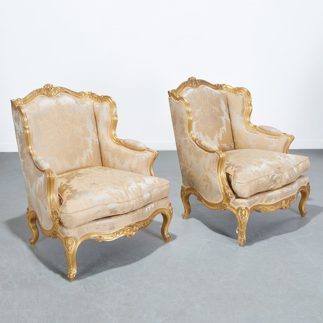 Nice pair Louis XV style giltwood bergeres: Nice pair Louis XV style giltwood bergeres, 20th c., bergeres a oreilles, with floral crest, serpentine seat with loose cushion, raised on foliate carved cabriole legs, upholstered in champagne