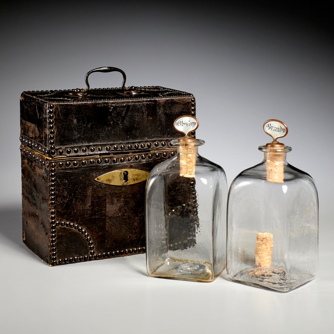 George III tacked leather spirits case: George III tacked leather spirits case, 18th c., two hand-blown decanters, mother-of-pearl "Whiskey" and "Brandy" stoppers, felt-lined travel case wrapped in leather with brass nail heads, handle and