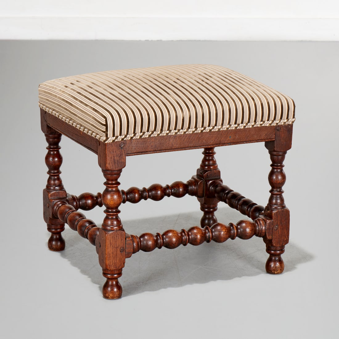 English Baroque turned oak stool: English Baroque turned oak stool, 18th c., with modern striped upholstery, 16"h 17.5"l x 15.5"w Provenance: The Collection of June and Frank Barsalona, NYC