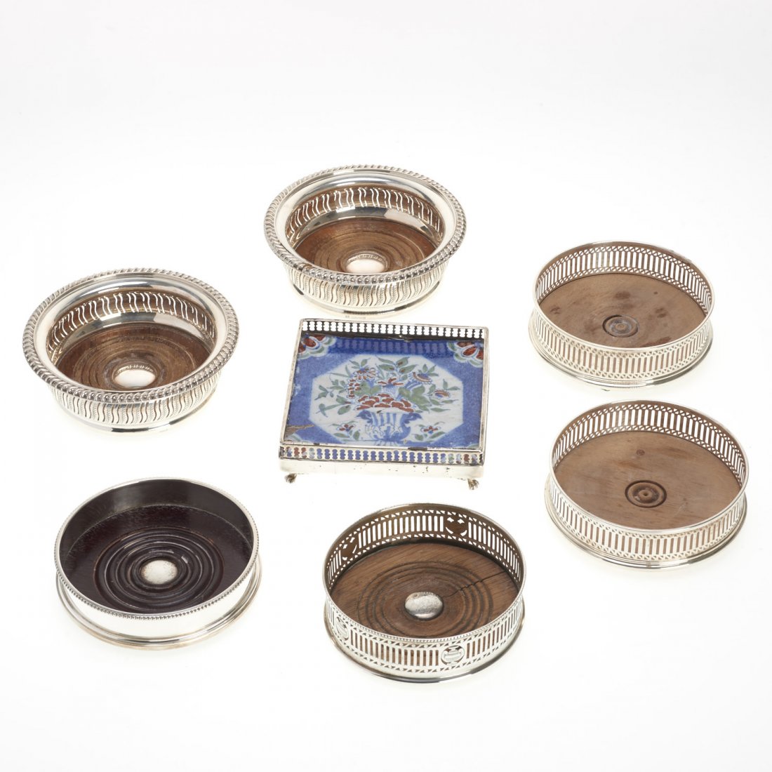 (7) English sterling wine coasters and trivets: (7) English sterling wine coasters and trivets, London and Birmingham, incl. pair by Baker, Ellis Silver Co., c. 1965, and Richard Comyns, c. 1920, trivet with inset Delft tile by Charles Mappin, c. 1