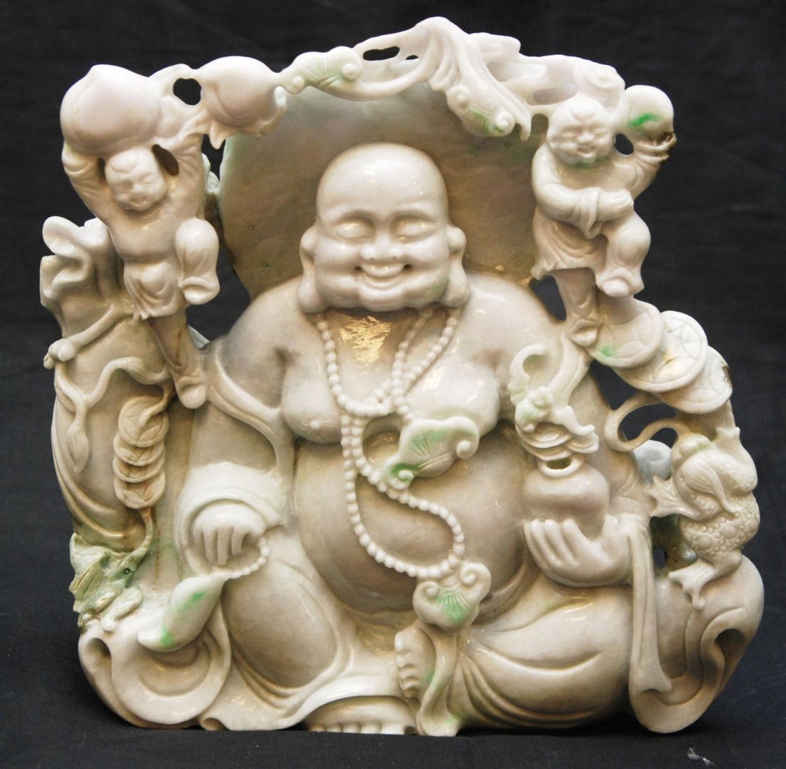 CHINESE CARVED JADEITE SCULPTURE OF SEATED BUDDHA Chine: Chinese fully relief carved jadeite sculpture depicting a seated happy Buddha. Next to him is his sack of belongings. Around him are two children holding peaches. Coins, bats, and lingzhi fungus with 
