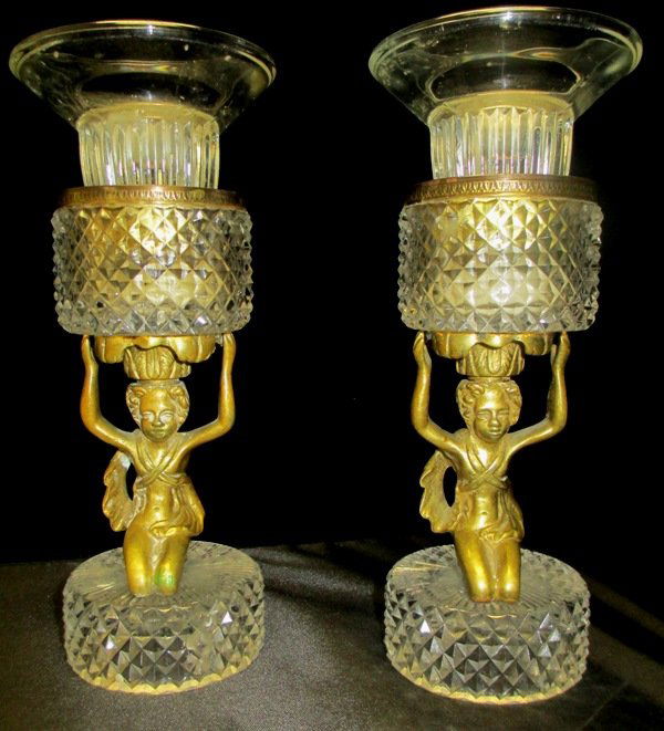 PAIR OF FRENCH BRONZE AND CRYSTAL CANDLESTICKS: Pair of French Gilt-Bronze and Rock Crystal Candlestick in the Louis XVI Taste, ca. 1900, each with a crystal modeled candle-cup supported by a Bronze Figurine joined to a stepped circular crystal bas