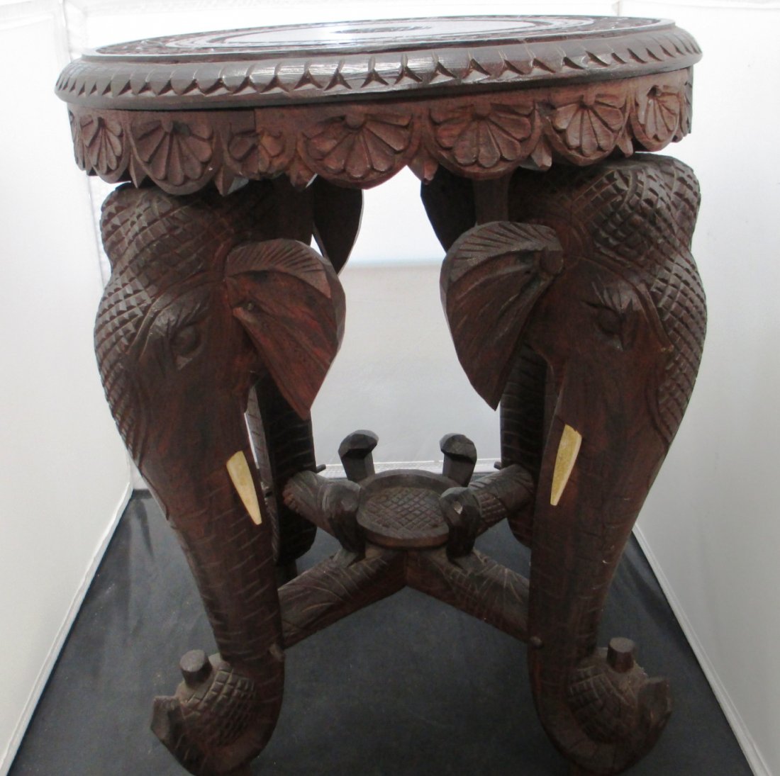HAND CARVED ENGRAVED WOOD ELEPHANT TABLE: HAND CARVED ENGRAVED WOOD ELEPHANT TABLE Fine Detail Floral Motiff on Top of Table. Base of Stool consists of 4 Elephant Heads with Trunks Up holding Bottles. Tusks are made of Bone Measures 15" Diame