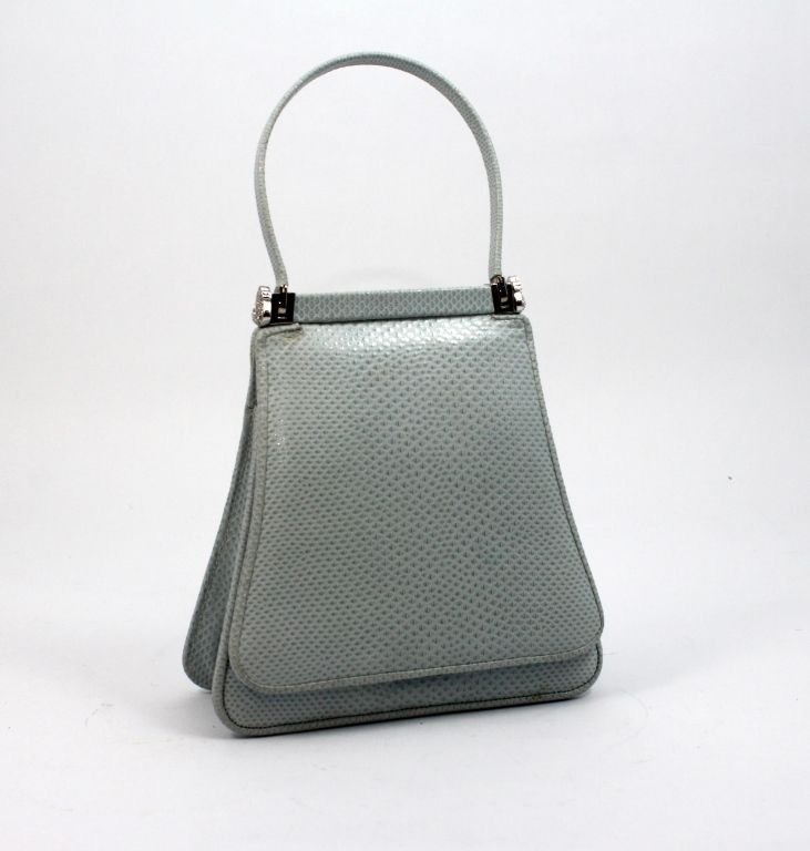 JUDITH LEIBER BLUE LIZARD SKIN LEATHER PURSE: A Judith Leiber light blue lizard skin jeweled purse. Blue silk interior with two pockets, one zippered. Includes comb and mirror. Measures 9" height including handle x 5 1/2" width.