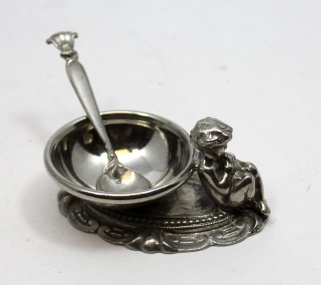ANTIQUE SILVERPLATE FIGURAL SALT CELLAR w SPOON: Antique silver plate figural open salt depicting a seated cherub on scrolled base. including a recast Wallace Romance of the Sea spoon. Late 19th to early 20th century. Measures 1 1/8" height x 2 3/8"