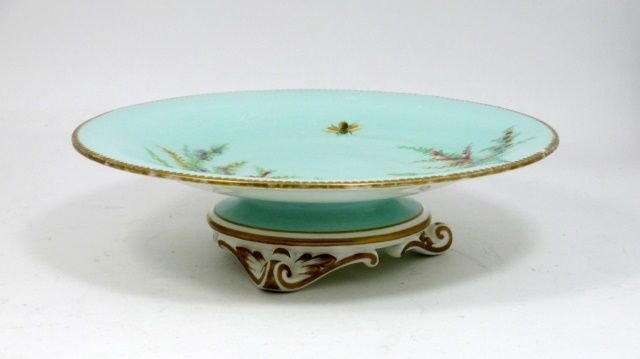 ANTIQUE MINTON ENGLISH PORCELAIN FOOTED PLATE: Antique Minton English porcelain compote depicting floral sprays with encroaching bee. Circa 1870's. Incised M mark to bottom and numbered. Measures 2 1/2" height x 9 1/8" diameter. Total weight of 66