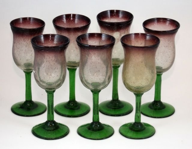 7pcs OF PATE DE VERRE STYLE STUDIO GLASS STEM CUPS: A set of seven hand blown amethyst to clear and emerald studio glass stem glasses having a Daum Pate de Verre. Each measures approx. 8 1/2" height. Total weight of approx. 2394 grams.