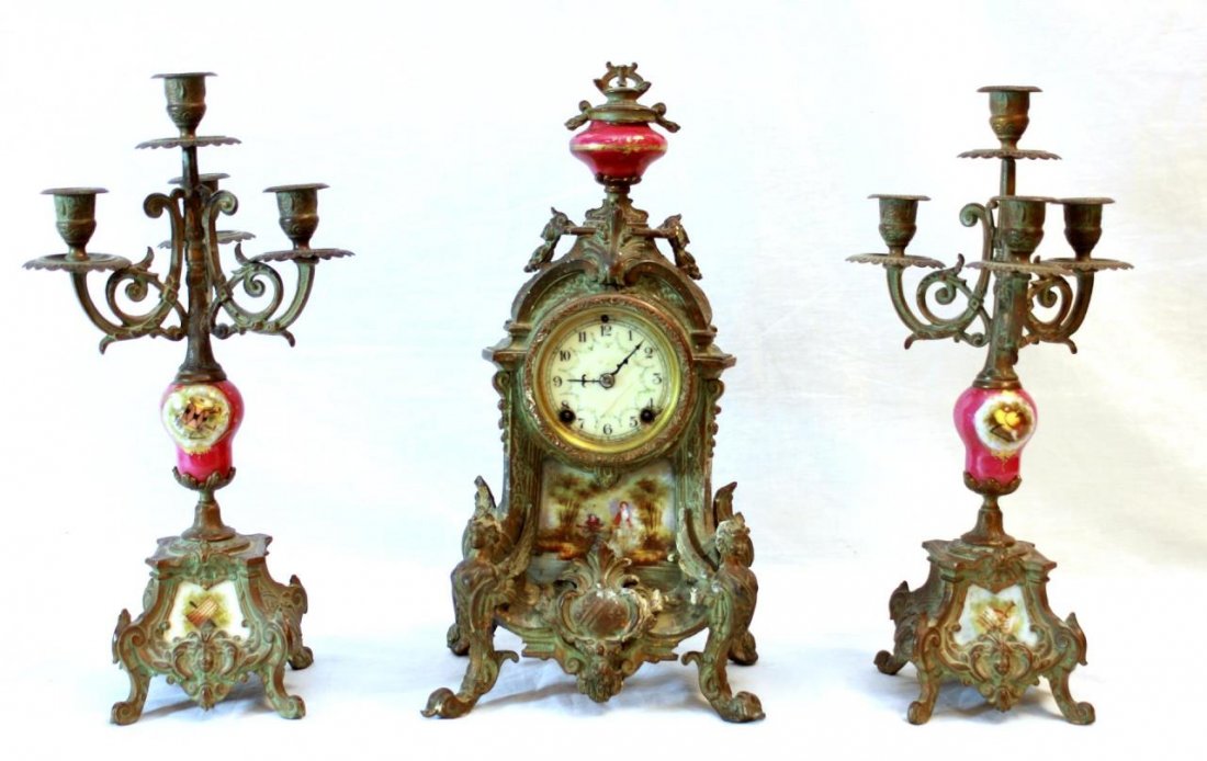 ANTIQUE FRENCH METAL PORCELAN CLOCK GARNITURE SET: Antique Continental three piece French metal and porcelain garniture set. Mounted with porcelain plaques having hand painted designs depicting courting couple and musical instruments. Ivory enamel fac