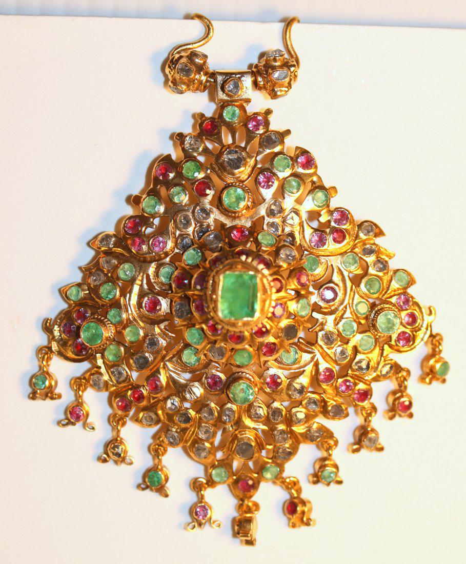 22K Yellow Gold Pendant Emerald, Ruby, Diamonds: 22k yellow gold, ceremonial style pendant in a curved and leaf design from India with a raised center. At the center is a bezel-set emerald, approximately 1.29ct. Surrounding are ten flush set rubies,
