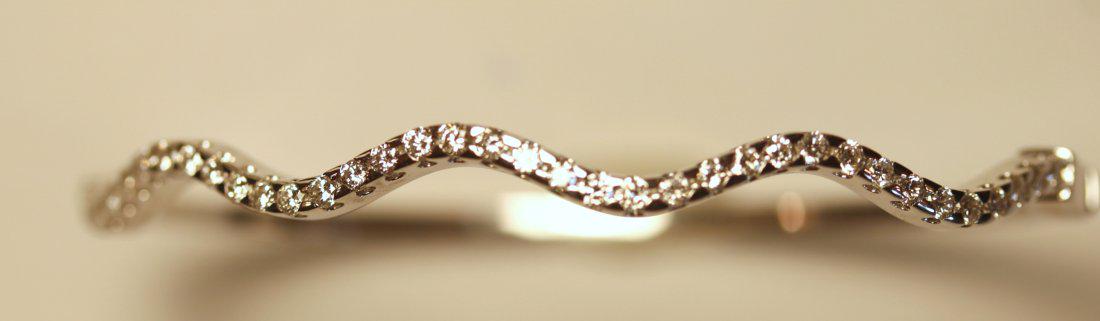 18K White Gold & Diamond Bangle Bracelet: 18k white gold bangle bracelet featuring thirty-nine prong set, round brilliant cut diamonds. Diamonds are set into a wave across the top of the bracelet. Hinge and insert clasp. TW of Diamonds: 1.23c