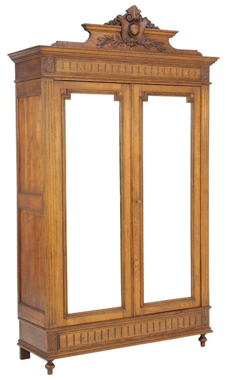 AN ANTIQUE OAK HENRI II TWO DOOR MIRRORED ARMOIRE: AN ANTIQUE OAK HENRI II TWO DOOR MIRRORED ARMOIRE Early 20th Century The cornice highlighted by a carved scrolling foliate motif surmounting a reeded frieze above a pair of beveled mirrored locking do