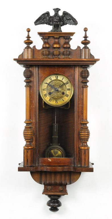 A VICTORIAN EMPIRE STYLE PENDULUM WALL CLOCK WITH EAGLE: A VICTORIAN EMPIRE STYLE PENDULUM WALL CLOCK WITH EAGLE Early 20th Century An eagle flanked by finials tops a Victorian Empire style wall clock featuring bronze finish pendulum and face flanked by tur