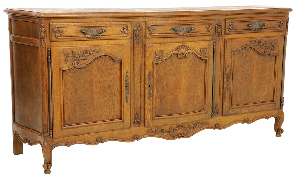 A LOUIS XV STYLE OAK ENFILADE BUFFET: A LOUIS XV STYLE OAK ENFILADE BUFFET Early 20th Century A Louis XV style oak enfilade having three doors and three drawers with bronze finish hardware, carved scroll form, flower and shell details, a 