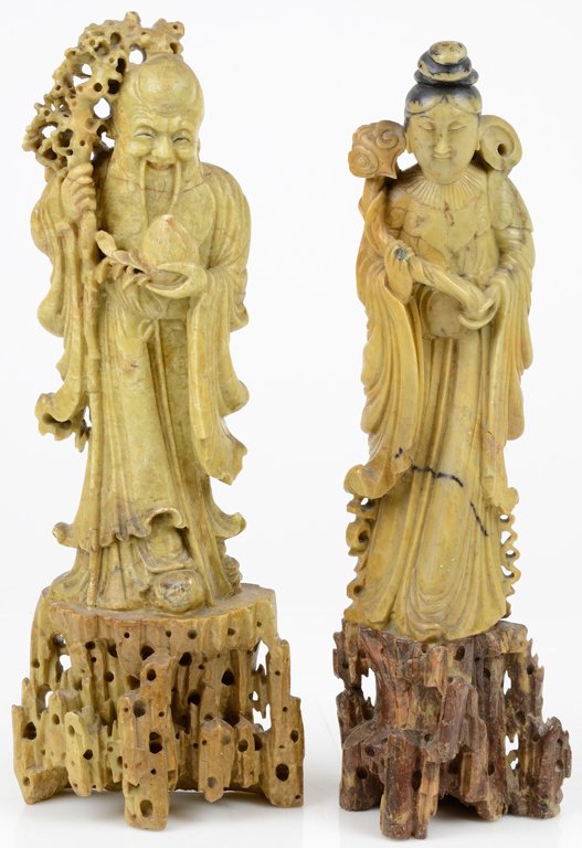 A PAIR OF CHINESE CARVED SOAPSTONE MALE AND FEMALE: A PAIR OF CHINESE CARVED SOAPSTONE MALE AND FEMALE FIGURES Minor chipping. Man holds a peach in his left hand and a gnarled staff in his right, woman holds a ruyi in right hand with base of scepter re