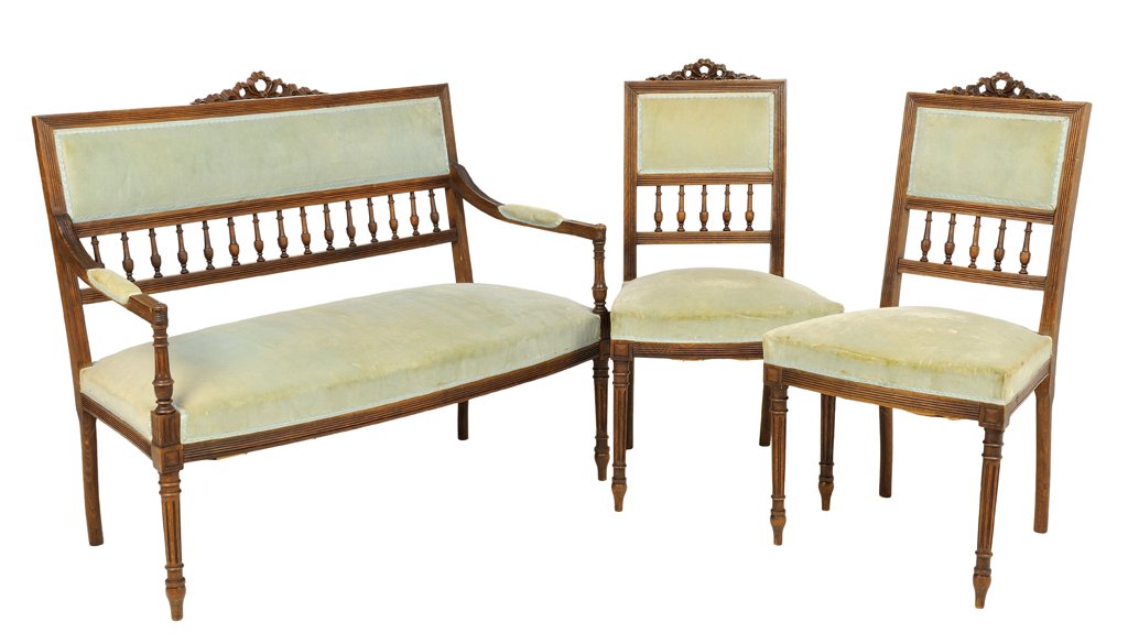 A FRENCH LOUIS XVI STYLE UPHOLSTERED WALNUT SALON SUITE: A FRENCH LOUIS XVI STYLE UPHOLSTERED WALNUT SALON SUITE The set comprising a settee and two side chairs, each having a carved ribbon-tied crest over upholstered back and seat, raised on fluted taperin