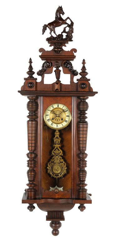 A VICTORIAN STYLE MAHOGANY WALL CLOCK: A VICTORIAN STYLE MAHOGANY WALL CLOCK The clock having a horse form finial over the pierce carved crest flanked by urn form finials above the circular enameled chapter ring having Roman numeral hours