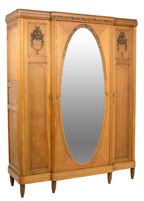 A FRENCH LOUIS XVI STYLE ARMOIRE: A FRENCH LOUIS XVI STYLE ARMOIRE The three door armoire fitted with an oval mirror plate, carved floral and urn decoration under the straight cornice, raised on tapering reeded legs. 87½ x 67½ x 23�