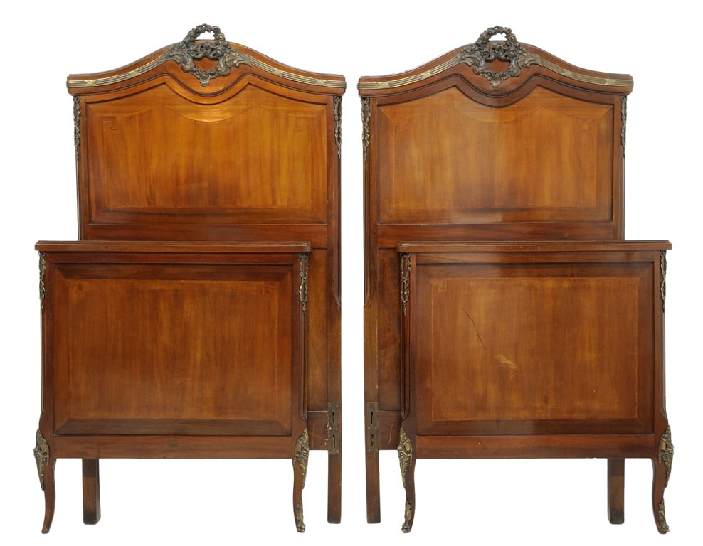 A PAIR OF FRENCH LOUIS XV STYLE WALNUT BEDS: A PAIR OF FRENCH LOUIS XV STYLE WALNUT BEDS The pair of beds crowned by a serpentine shaped top mounted with gilt bronze wreath, inlaid banded headboard flanked by ribbon-tied wreaths. The footboard r