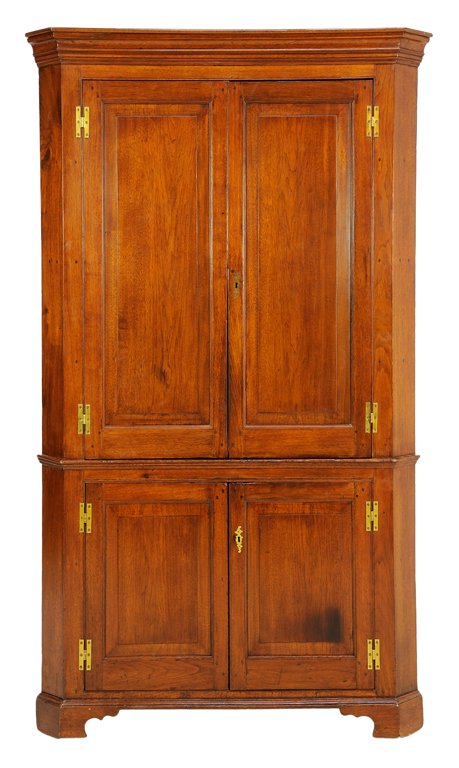 AN AMERICAN FEDERAL STYLE WALNUT CORNER CABINET: AN AMERICAN FEDERAL STYLE WALNUT CORNER CABINET The cabinet having two long paneled doors over two short paneled doors, with a flared cornice, opening to a shelved interior, raised on bracket feet. 81