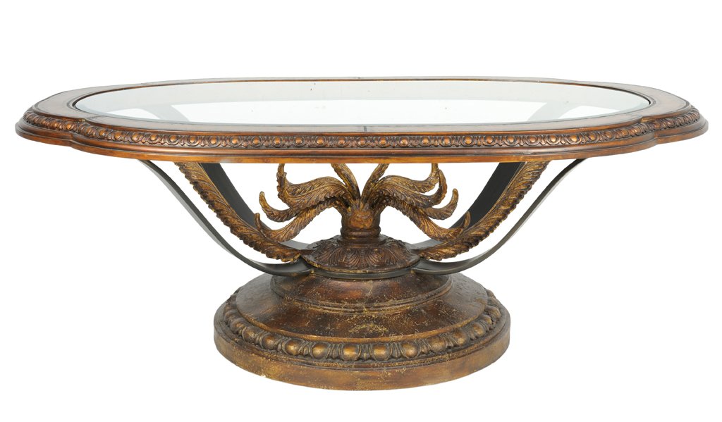 A CONTEMPORARY NEOCLASSICAL STYLE CARVED LOW TABLE: A CONTEMPORARY NEOCLASSICAL STYLE CARVED LOW TABLE The table having a lobed oval glass inset top, raised on a series of supports centered with scrolling leaves, ending in a stepped circular base. 23 x