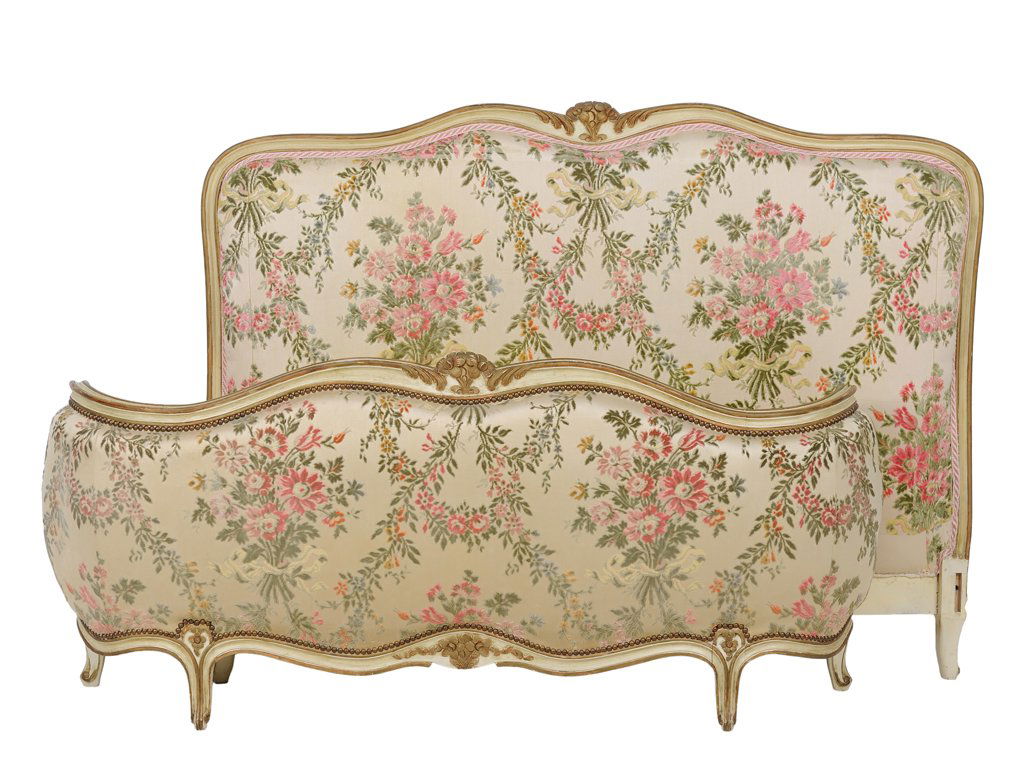 A FRENCH LOUIS XV STYLE UPHOLSTERED BED: A FRENCH LOUIS XV STYLE UPHOLSTERED BED The headboard and footboard having a curved top rail centered with gilt painted flowers, foliate upholstery with nailhead trim, above the shaped apron, raised o