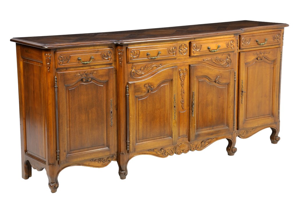 A FRENCH PROVINCIAL STYLE WALNUT SIDEBOARD: A FRENCH PROVINCIAL STYLE WALNUT SIDEBOARD The sideboard having a shaped rectangular top over four short drawers and four paneled doors, coffer paneled side, above the serpentine carved apron, raised 