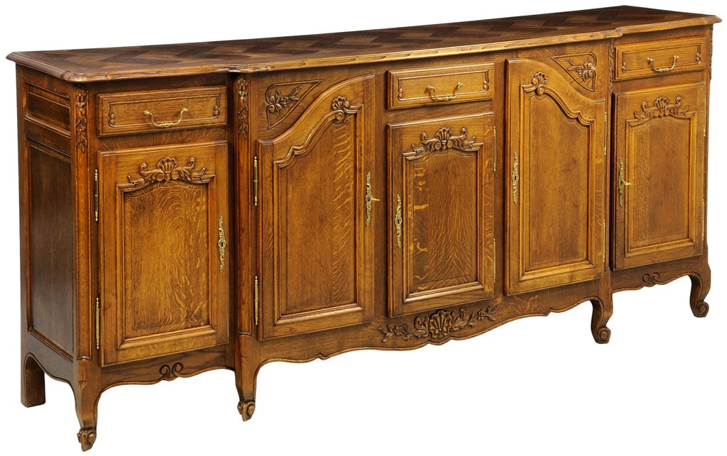 A FRENCH PROVINCIAL STYLE WALNUT SIDEBOARD: A FRENCH PROVINCIAL STYLE WALNUT SIDEBOARD The sideboard having a shaped rectangular top over three short drawers and five paneled door, coffer paneled sides, above the serpentine apron centered with 