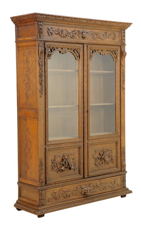A RENAISSANCE REVIVAL VITRINE CABINET: A RENAISSANCE REVIVAL VITRINE CABINET The vitrine cabinet having a flared cornice over the foliate carved frieze, above two glazed doors, opening to a shelved interior, carved with musical trophy deco