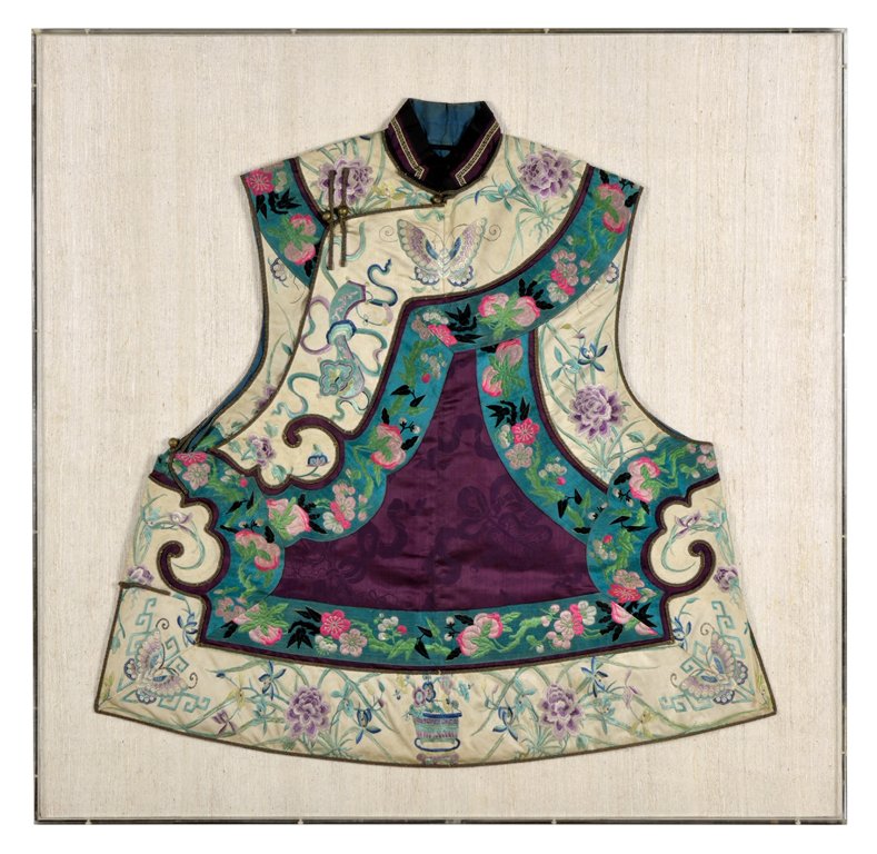 A CHINESE EMBROIDERED TEXTILE: A CHINESE EMBROIDERED TEXTILE The lady's shirt or vest having embroidered Greek key motif at the collar, the neck and shoulder with corded closures and brass fittings, above the body panels of cream, 