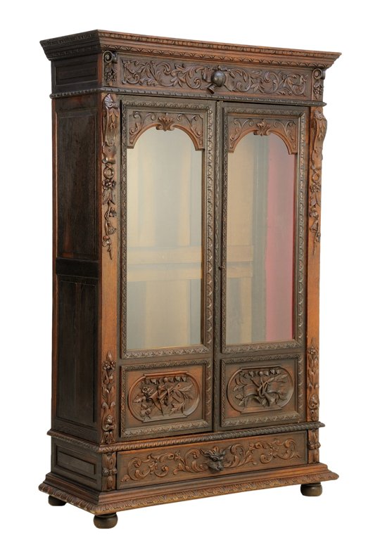 A FRENCH RENAISSANCE REVIVAL VITRINE CABINET: A FRENCH RENAISSANCE REVIVAL VITRINE CABINET With a flared cornice over the foliate carved frieze, atop a pair of glazed double doors ending in panels carved with musical trophy decorations, over a si