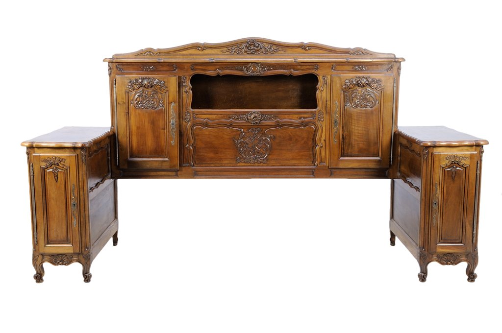 A FRENCH PROVINCIAL STYLE HEADBOARD AND BEDSIDE: A FRENCH PROVINCIAL STYLE HEADBOARD AND BEDSIDE CABINETS The headboard having a curved crest rail with carved foliate decoration over two paneled doors, flanked by bedside cabinets, each fitted with a
