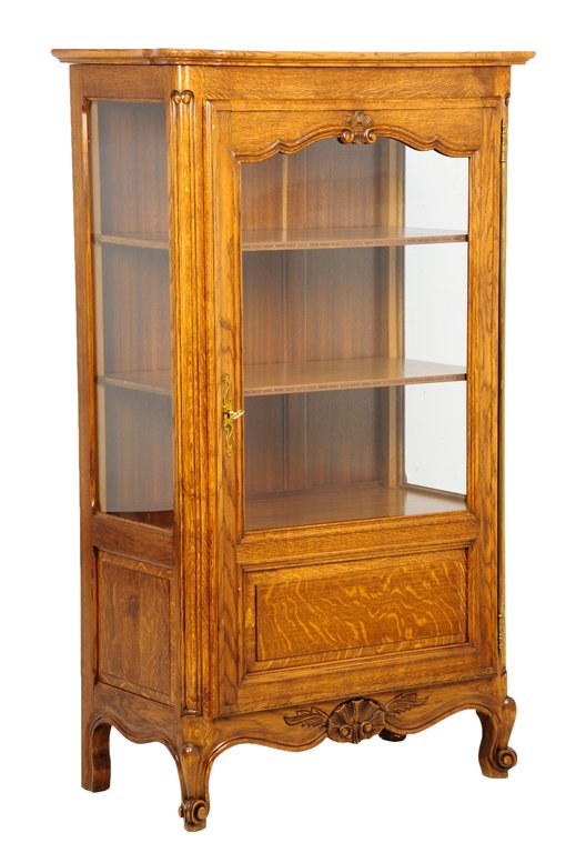 A FRENCH PROVINCIAL STYLE VITRINE CABINET: A FRENCH PROVINCIAL STYLE VITRINE CABINET The vitrine cabinet having a flared cornice over the glazed door and sides, opening to a shelved interior, above the serpentine apron, centered with a shell, 