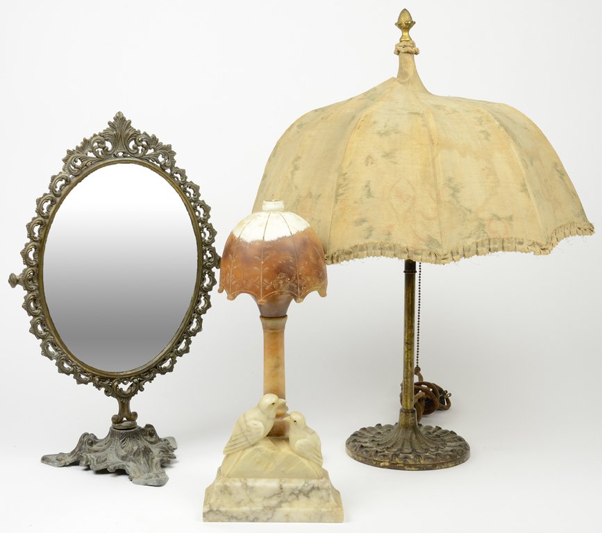 A GROUP OF DECORATIVE DRESSING ROOM ITEMS 3 pieces: A GROUP OF DECORATIVE DRESSING ROOM ITEMS The group comprised of a carved alabaster lamp, a gilt metal vanity mirror, and a table lamp. 3 pieces total H 24¾ x diam 18 inches.
