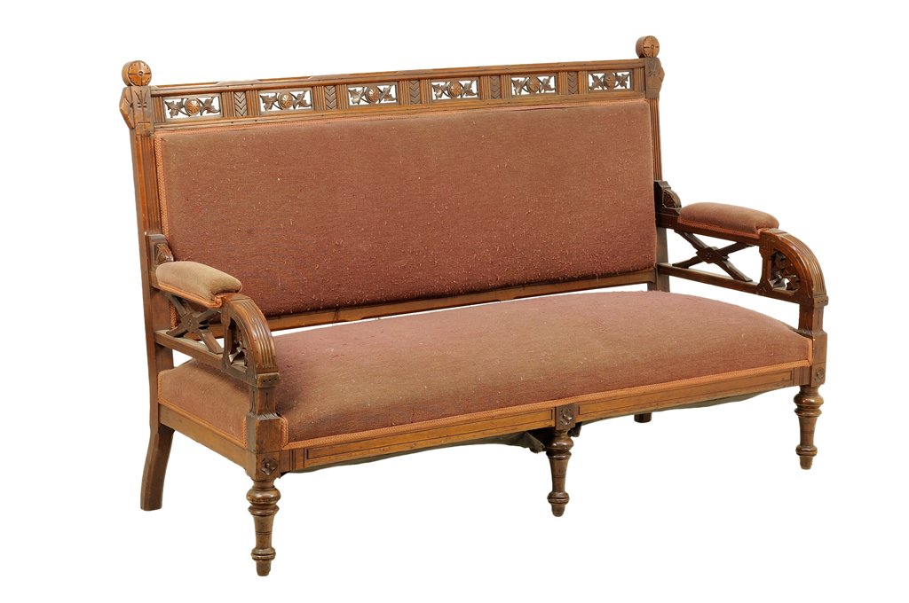 AN AESTHETIC STYLE UPHOLSTERED SETTEE: AN AESTHETIC STYLE UPHOLSTERED SETTEE The settee having a pierce carved crest rail flanked by rosette finials, over the upholstered back and stuff-over seat, within open arms, raised on cylindrical ta