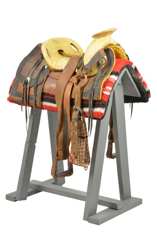 A MEXICAN VAQUERO SADDLE: A MEXICAN VAQUERO SADDLE Having a tooled leather skirt and fender, the rear saddle pockets with ebonized trim and silvered metal fittings, and surmounted by the wood seat with stamped mark Fusteria "L