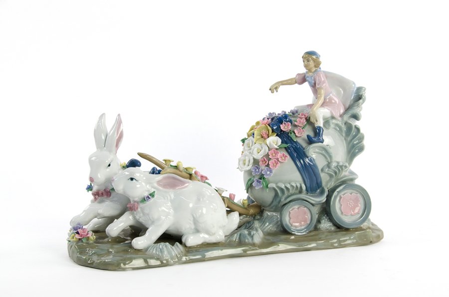 A FARINELLI PORCELAIN FIGURAL GROUP: A FARINELLI PORCELAIN FIGURAL GROUP 20th century The figural group depicting two rabbits pulling a sprite on an egg form carriage, with applied flowers throughout, raised on a naturalistic oval base, 